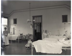 nurse and three children (one in a small rocking chair and two in bed) the an isolation ward at a children's hospital.