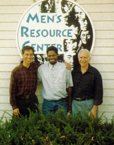 3 men, Steven Botkin, Thulani Nkosi, and Rob Okun in front of a sign for the Men's Resource Center