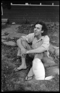 Tom Fels seated on the ground in flip flops at the Montague Farm