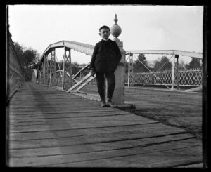 photograph of a boy standing next to a post on a bridge