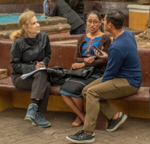 Julia Lieblich seated on a bench with a notebook listening to Maya actress Maria Mercedes Coroy