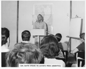 Colonel William M Smith speaks at a podium before an assembled group of people from Argentina.